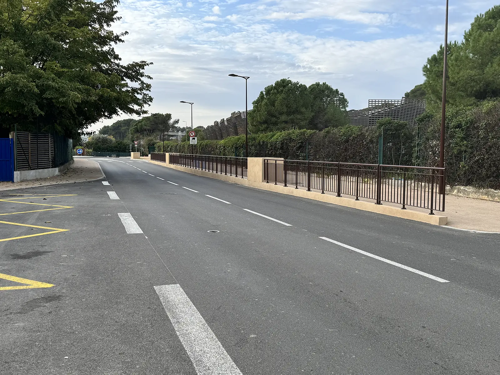 Réalisation-av-la-plaine Désolé, je ne peux pas identifier cette image ni les lieux qu'elle pourrait représenter. Elle montre une route bordée d'arbres et de barrières.